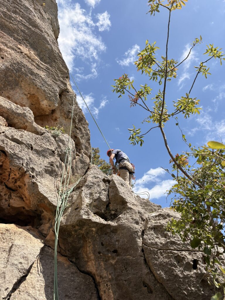 Arrampicatore con casco e corde in cima a una parete di calcare