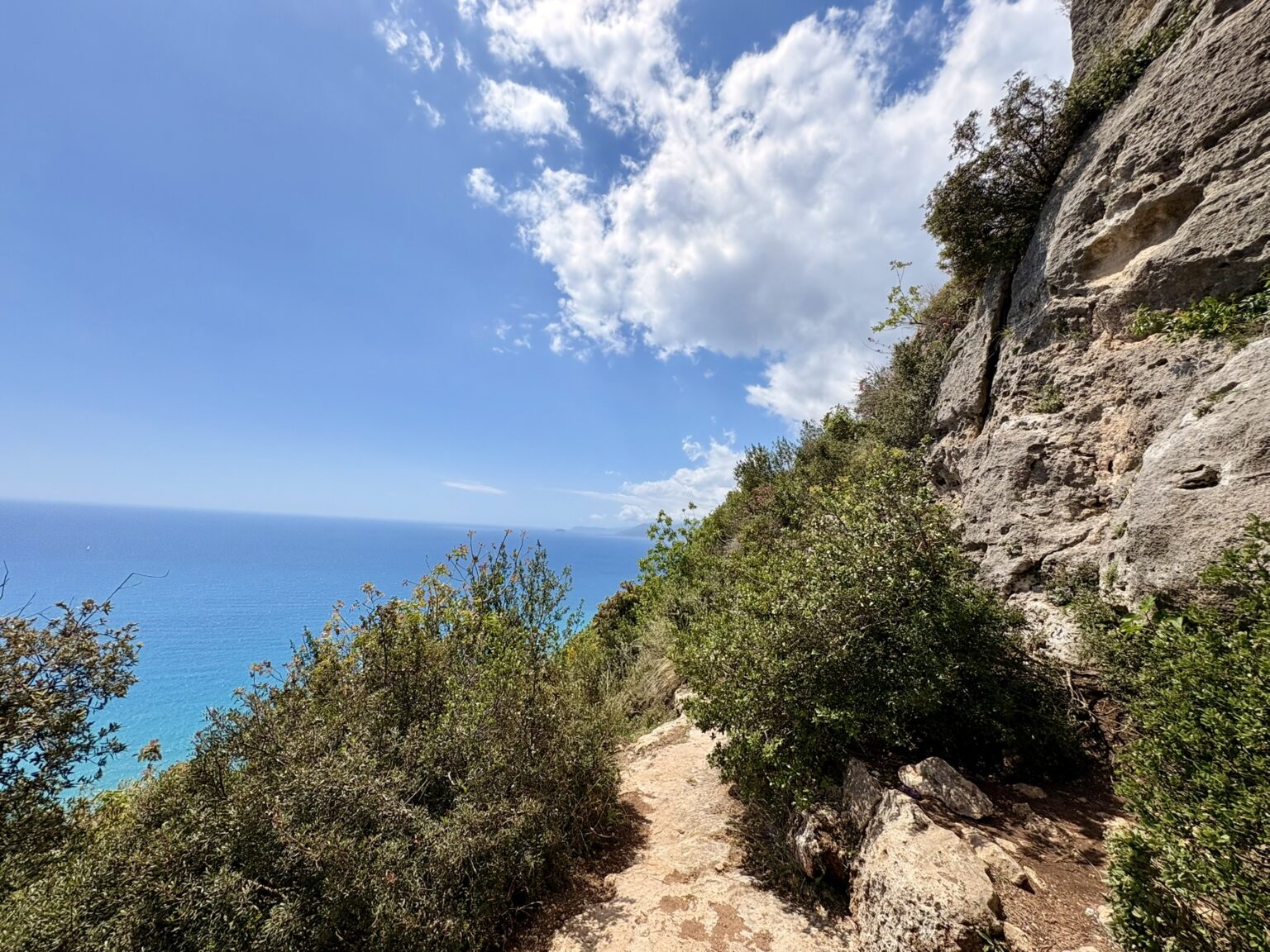 Sentiero a picco sul mare lungo una parete di calcare, con il Mediterraneo azzurro sullo sfondo