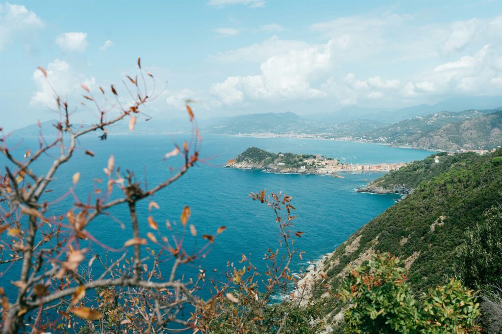 Costa ligure vista dall'alto tra rami dai colori d'autunno, con il mare azzurro e un promontorio con un borgo